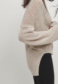 Beige gestrickter Pullover mit lockerer Passform und weiten Ärmeln. Verfügt über einen tiefen V-Ausschnitt und ein asymmetrisches Saumdesign. Das strukturierte Garn sorgt für ein atmungsaktives Erscheinungsbild.