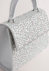 Bolso plateado cubierto de brillantes cristalinas con un diseño estructurado, forma rectangular y doble asa, con una textura suave.
