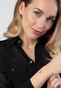 Gold heart-shaped necklace and bracelet on a model. The necklace features a delicate chain, while the bracelet has a small heart charm.