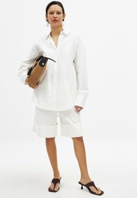 White oversized shirt, glossy white shorts with folded cuffs, brown minimalist handbag, and brown heeled sandals. Smooth fabric texture.