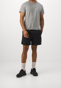 Camiseta deportiva gris de manga corta, pantalones cortos negros, calcetines blancos y zapatillas negras. Presenta el logo de Nike en la camiseta y los pantalones cortos.