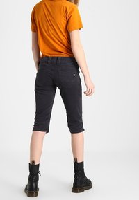 Pantalones recortados negros con un ajuste slim, combinados con una camiseta naranja. Los pantalones tienen bolsillos traseros y se llevan con botas de tobillo negras.