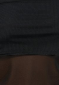 Κοντινό πλάνο σκουρόχρωμου δίχρωμου υφάσματος με μαύρο δίχτυ πάνω από σκούρο καφέ υλικό, που δείχνει υφή και λεπτομέρειες ραφής.