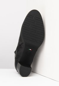 Chaussure en cuir noir avec un petit talon carré, semelle en caoutchouc texturée et détail de fermeture éclair sur le côté arborant les couleurs du drapeau italien.