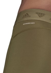 Olijf groene Adidas tights met een getextureerde tailleband, voorzien van het logo en "AEROREADY" in het wit gedrukt. Gladde stof met platte naden.