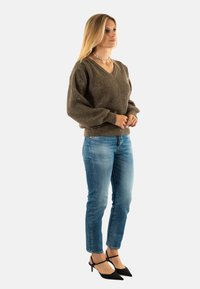Maglione a maglia marrone testurizzato con scollo a V e maniche a palloncino, abbinato a jeans slim blu chiaro e décolleté neri a punta.
