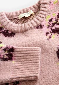 Adīta džemperis gaiši rozā krāsā ar ribotu apkakli un piedurknēm. Iekļauj ziedu rakstu tumši purpursarkanā un zaļā krāsā. Mīksta tekstūra. Redzama zīmola etiķete.