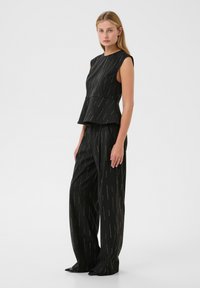 Czarny top peplum i szerokie spodnie z metalicznymi złotymi pionowymi akcentami. Gładka textura, dopasowany krój, bez rękawów i wysoki dekolt.