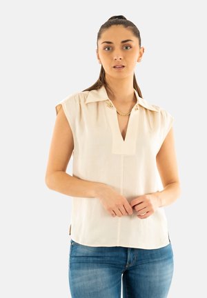 Blusa beige de manga corta con cuello de muesca, ligera gather en los hombros y aberturas laterales. La tela parece ligera y suave.