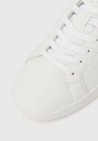 Fehér bőrből készült sportcipő lekerekített orral, lapos fehér fűzőkkel, finom varrási részletekkel és texturált gumi talppal.