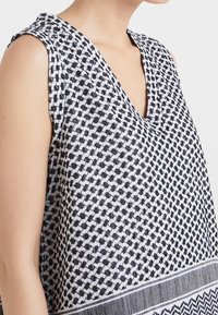 Vestido sin mangas con escote en V, confeccionado en una tela ligera con un patrón geométrico en blanco y negro y un dobladillo horizontal en contraste.