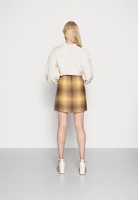 Top puff-sleeve color beige chiaro abbinato a una gonna mini aderente con un motivo a quadri giallo e marrone, completato da scarpe con tacco a blocco bianche.