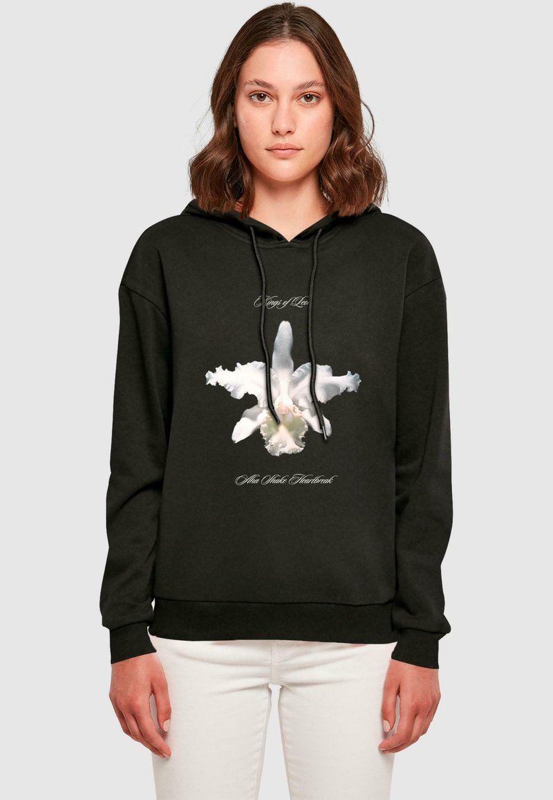 Svart hoodie med en vit orkidé grafisk tryck och text. Materialet verkar mjukt, med dragsko i huvan och ribbade muddar.