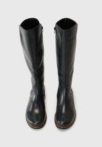 Bottes noires en cuir montantes avec une finition lisse, un bout rond et des zips latéraux. Semelle extérieure marron robuste avec une légère texture.