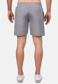 Shorts de bain gris avec une taille élastique, une poche arrière et une texture lisse. Portés avec des baskets blanches et une longueur visible jusqu'à la cheville.
