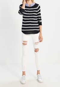 Suéter de punto a rayas blanco y negro con cuello redondo, combinado con jeans skinny blancos desgastados y zapatos slip-on blancos.