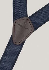 Granatowe szelki z tkaniny z brązowymi skórzanymi akcentami oraz trójkątną łatą wytłoczoną napisem "PROCHNIK". Trwały i teksturowany materiał.