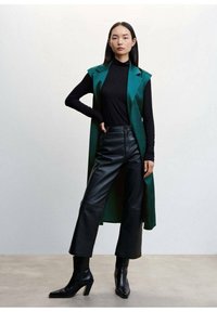 Długi turkusowy kamizelka noszona na czarnym golfie, dopełniona spodniami skórzanymi o wysokim stanie w kolorze czarnym oraz eleganckimi czarnymi botkami za kostkę.