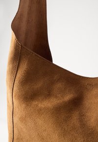 Brown suede shoulder bag with a smooth texture and rounded shape. Features simple stitching and a wide strap for easy carrying.