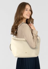 Borsa a spalla in pelle color crema con una texture liscia, dalla forma strutturata, caratterizzata da un logo in tonalità oro e una singola tracolla regolabile.
