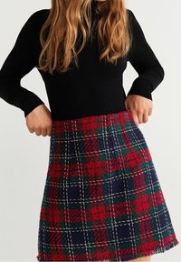 Jupe à carreaux rouge, verte et marine. Coupe trapèze en tissu texturé avec ourlet à franges et surpiqûres blanches contrastantes.