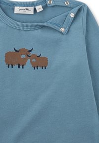 Blaues Langarmhemd aus weichem Stoff mit einem braunen und schwarzen Grafik von zwei Kühen auf der Vorderseite, mit Druckknöpfen an der Schulter.