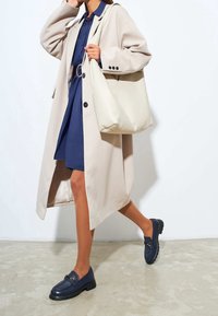 Beige lång kappa, marinblå skjortklänning och marinblå loafers. Krämfärgad väska, glänsande detaljer på skorna, släta texturer och strukturerade silhuetter.