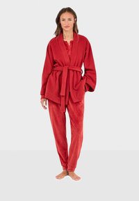 Conjunto de loungewear de terciopelo rojo que incluye una bata holgada con cinturón y pantalones a juego adornados con sutiles detalles.