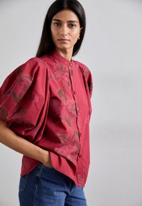 Rotes Hemd mit Puffärmeln und einem Blumenmuster in Rosa- und Brauntönen, kombiniert mit blauen Jeans.