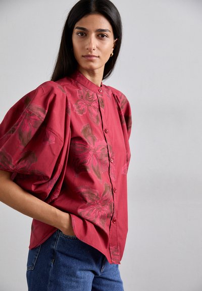 Red button-up shirt with puffed sleeves and floral print in shades of pink and brown, paired with blue denim jeans.
