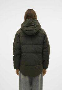 Giacca a vento verde con cappuccio, caratterizzata da un design trapuntato e una parte posteriore leggermente allungata. Il materiale appare liscio e leggero.