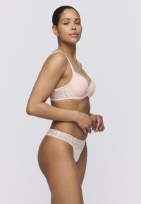 Reggiseno di pizzo e perizoma coordinato in un delicato rosa. Il reggiseno presenta ferretto, bordi ondulati e motivi floreali. Il perizoma ha un bordino di pizzo lungo la vita.