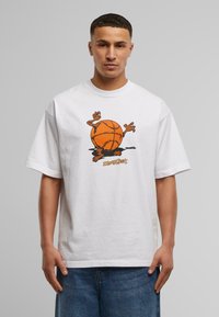 Hvit bomull t-skjorte med en grafikk av en oransje basketball med tegneseriearmer, satt mot en nøytral grå bakgrunn.