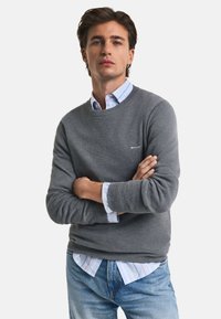 Grau strukturierter Pullover mit Rundhalsausschnitt, über einem hellblauen und weißen gestreiften Hemd mit Knöpfen. Verstellbare Manschettendetails. Lässige Passform.