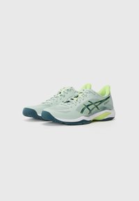 Des chaussures de sport vert clair avec une tige en mesh, des accents vert foncé, une semelle texturée et un talon vert lime. Conçues pour la performance.