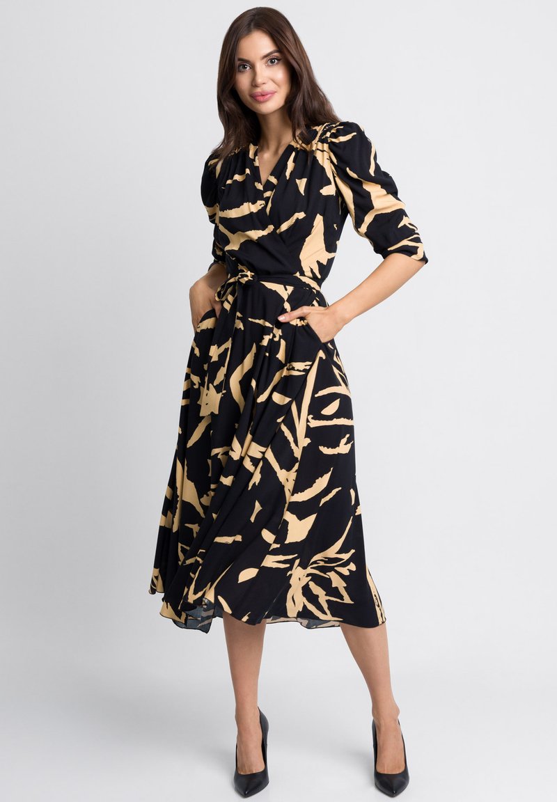 Czarna sukienka z beżowym abstrakcyjnym wzorem, bufiastymi rękawami i paskiem w talii. Tkanina ma gładką fakturę i posiada boczne kieszenie.