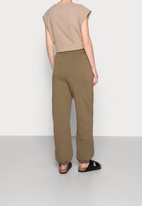Camiseta corta beige con mangas remangadas combinada con pantalones deportivos verdes oliva. La modelo lleva sandalias negras, mostrando un tejido suave y un ajuste relajado.