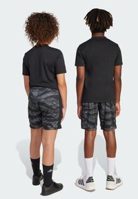 Svarta t-shirts parats med svarta kamoflagshorts. Båda har på sig svarta skor och strumpor. En har vita strumpor och skor med svarta accenter.