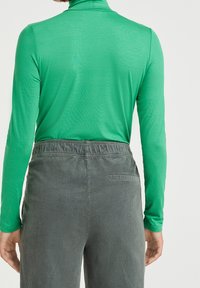 Grön långärmad polotröja kombinerad med mörkgrå kordflorsbyxor. Toppen har en slät, elastisk textur och en tight passform.