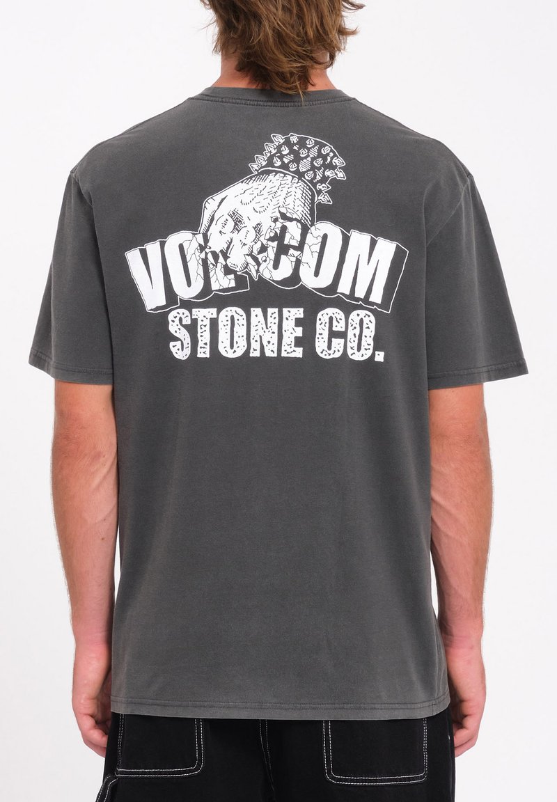 Camiseta de algodón gris con un gran gráfico blanco de una calavera y el texto "VOLCOM STONE CO." en la parte trasera. Mangas cortas, cuello redondo.