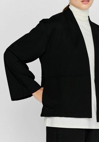 Zwarte open shirtjas met brede mouwen, gemaakt van zachte stof. Simplistisch ontwerp met een horizontale naad en een ontspannen pasvorm.