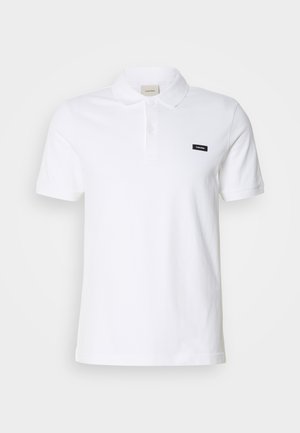 Biała bawełniana koszulka polo z klasycznym kołnierzykiem, krótkimi rękawami i małym czarnym logo Calvin Klein na lewej piersi.