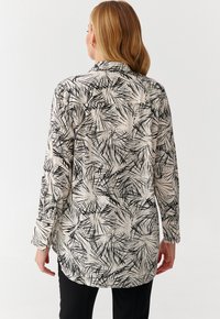 Langelangem blouse met een zwart-wit abstract bladerenpatroon, lichte stof, met knoopmanchetten en een licht gebogen zoom.