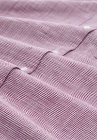 Tejido texturizado en color rosa claro con un pequeño patrón de cuadros, presentado con botones blancos a lo largo de un diseño doblado.