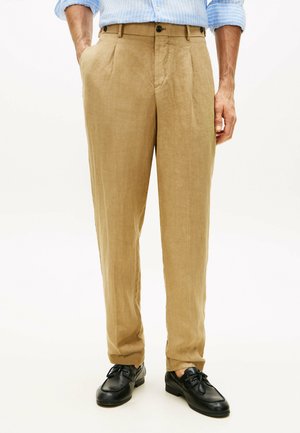 Mann trägt beige Leinenhosen, schwarze Leder-Schnürschuhe und ein blau gestreiftes Hemd mit hochgekrempelten Ärmeln.