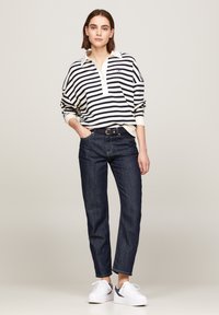 Sweter w paski w kolorze kremowym i granatowym z kołnierzykiem, w zestawieniu z ciemnoniebieskimi dżinsami i białymi sneakersami, o minimalistycznym designie i luźnym kroju.