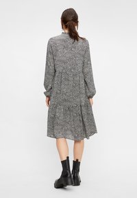 Vestido de patrón blanco y negro con mangas largas abullonadas, diseño de capas y cuello alto. Llevado con botas negras hasta el tobillo.