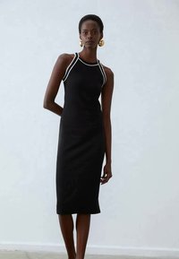 Vestido preto sem mangas com acabamento branco na gola, silhueta ajustada, comprimento até ao joelho, textura suave e design minimalista.