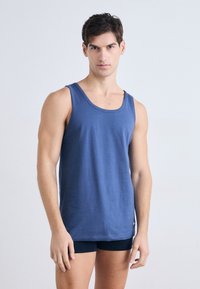 Tums zilgans kokvilnas topiņš ar plašu dekoltē un minimālu stiepšanos, apvienots ar tumšām biksēm. Gluda tekstūra, pieguļošs dizains bez rakstiem.