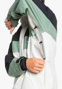 Farbenblockierte Jacke mit grünen, schwarzen und weißen Paneelen. Hergestellt aus leichtem, strukturiertem Material mit Reißverschlussbelüftungen und Klettverschlussärmelbündchen.